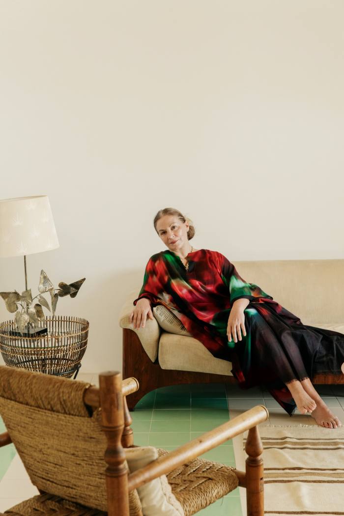 Kapoor siede su un divano degli anni '70.  Il tavolino e la lampada in rattan degli anni '60 provengono entrambi dal mercato di antiquariato di Alfies.  La sedia in rattan e legno è nello stile di Charlotte Perriand