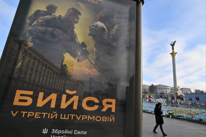 Una donna passa davanti a un poster raffigurante militari ucraini che combattono con scheletri dall'aspetto malvagio