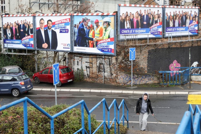 Una donna passa davanti a un cartellone elettorale a Belgrado che mostra il presidente serbo Aleksandar Vučić con i membri del partito progressista serbo al governo