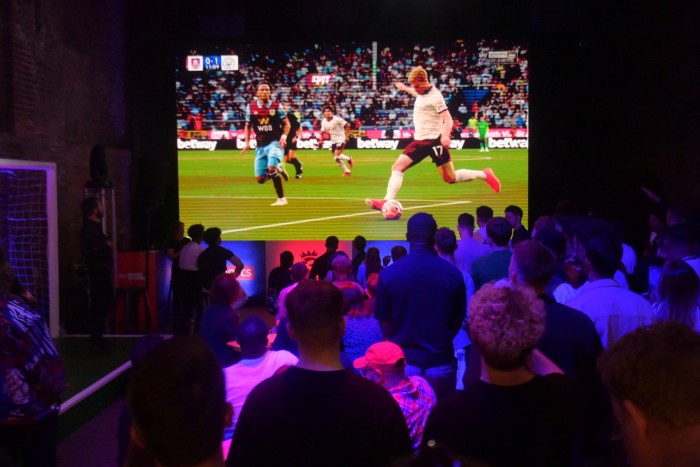 Il pubblico guarda uno schermo che mostra una partita di calcio