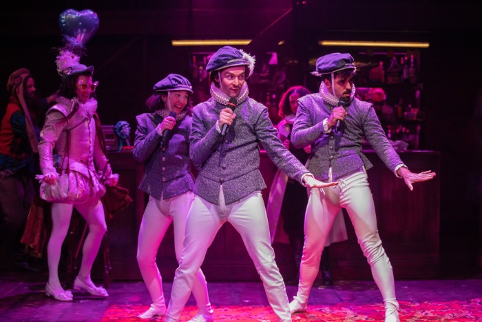 Un gruppo di persone in costume elisabettiano esegue una routine di danza cantando nei microfoni