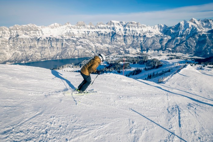 Uno sciatore con una giacca gialla su una pista a Flumserberg. In lontananza si vedono un lago e montagne innevate