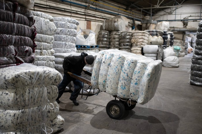 Un uomo in un magazzino usa un carrello per sollevare un'enorme balla di lana tinta