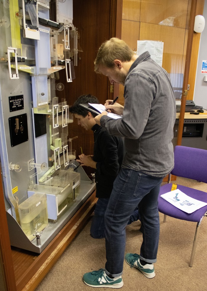 Due colleghi dell'agenzia di design digitale WongDoody stanno prendendo le misure di una macchina originale Phillips a Cambridge. Uno sta usando un metro a nastro, l'altro sta scrivendo su una lavagna