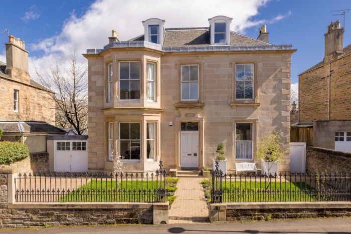Vista frontale di una casa indipendente costruita in arenaria chiara comune alle case scozzesi del XIX secolo, con un piccolo giardino erboso anteriore, un sentiero, un vialetto e un garage  