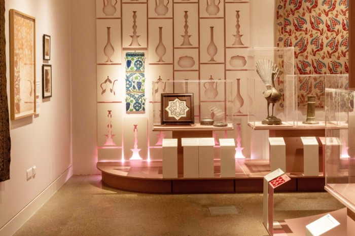 Una stanza di una mostra è piena di manufatti di origine o influenza mediorientale, tra cui piastrelle a motivi geometrici e un pavone di ottone