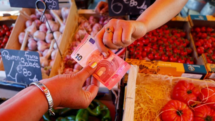 A shopper hands over a €10 banknote to a vendor at a local market in Nice, France