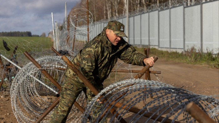 A guard opens a barbed wire gate near the Polish-Belarusian border