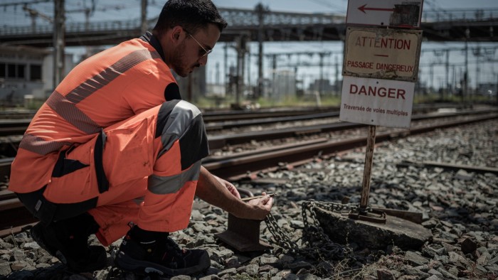 An employee, wearing an orange safety uniform, checks the temperature of railway tracks