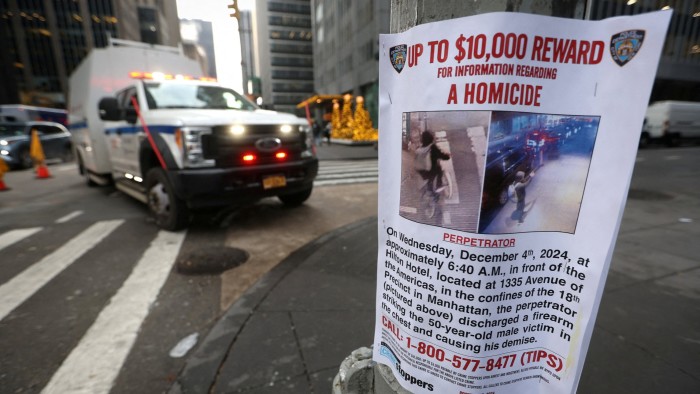 Ambulance drives by a poster outside the Hilton hotel near the scene where Brian Thompson was shot dead in New York City