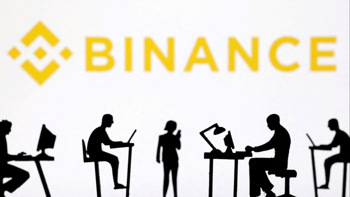Figurines with computers and smartphones are seen in front of Binance logo