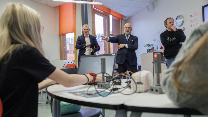 Three men talk in front of a classroom of students using laptops in Estonia