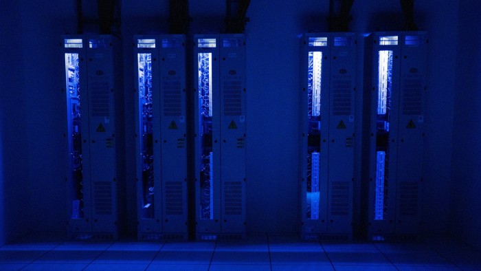 A bank of five stacks of computer hardware attached to thick cables and glowing in the dark