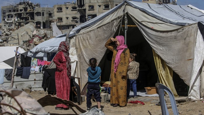 Palestinian women and children stand outside their tents among the rubble of destroyed buildings in Jabalia in northern Gaza