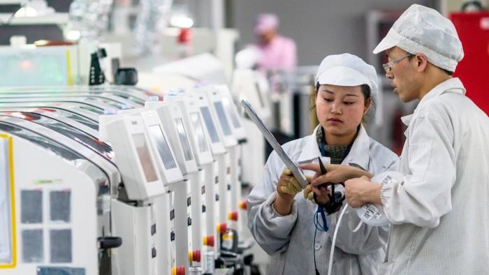 Two workers in cleanroom suits and caps operate machinery at a Foxconn factory in China