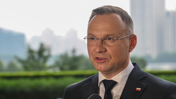 Polish President Andrzej Duda speaks at a press briefing. He is wearing a suit and tie, with a Polish flag pin on his lapel
