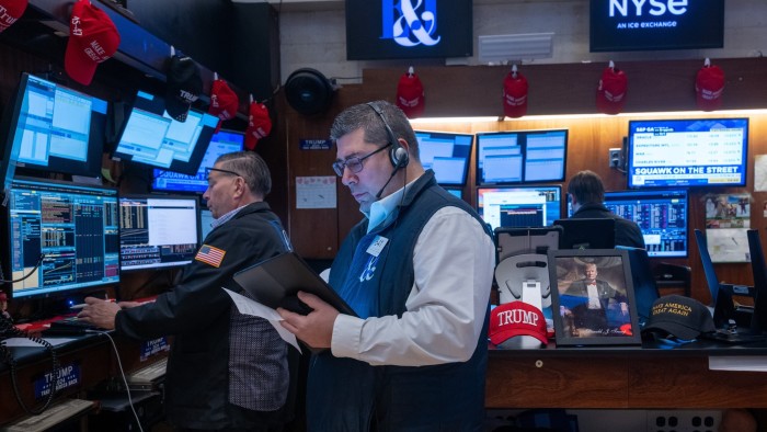Traders work on the New York Stock Exchange next to a Donald Trump picture