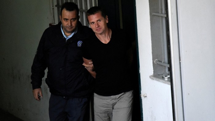 Alexander Vinnik is escorted by a police officer through a doorway