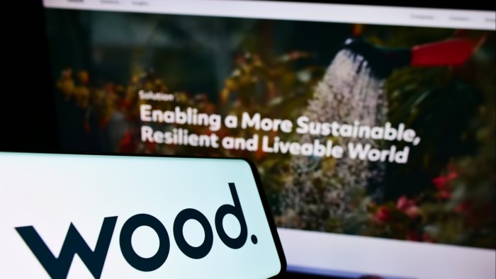 Mobile phone with logo of British engineering company John Wood Group in front of computer with its website