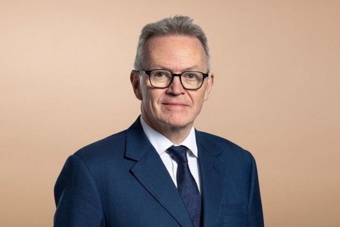 La sedia di Barclays Nigel Higgins contro uno sfondo beige