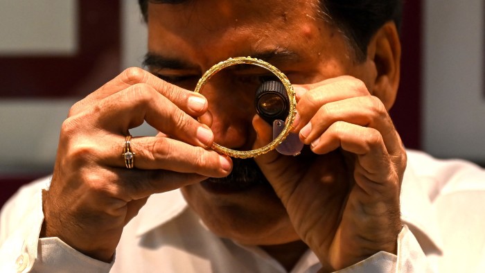 A shop manager using a loupe magnifying glass to inspect a gold bangle at a jewellery shop in Mumbai