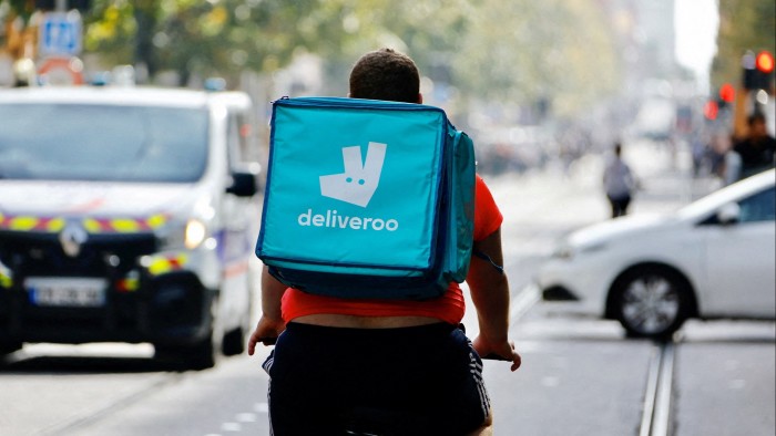 A Deliveroo delivery worker on a bike and wearing a backpack