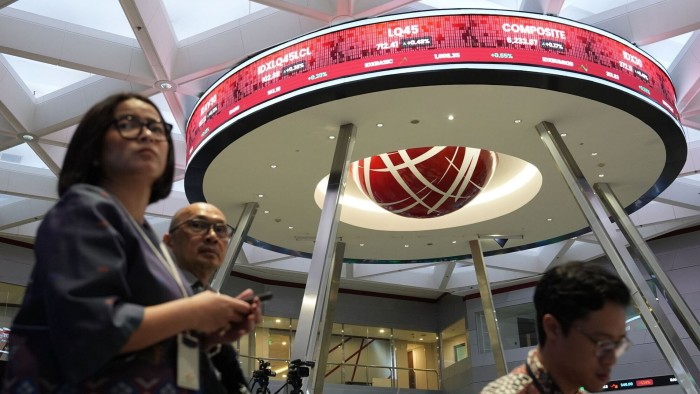 People walk in the Indonesia Stock Exchange, with a circular display board showing stock market information above them