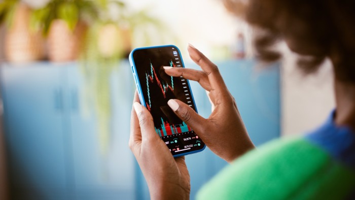 A woman watches stock charts on her smartphone