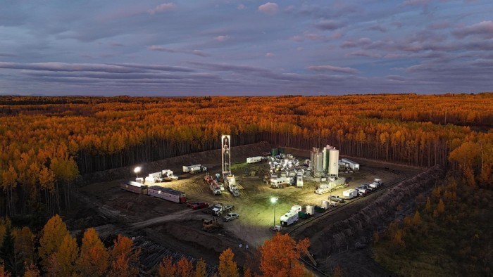 Oil or gas drilling site brightly lit in a clearing, surrounded by dense autumn forest with orange foliage