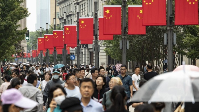 Crowds of people walk along Nanjing East Road in Shanghai, China, beneath rows of Chinese flags