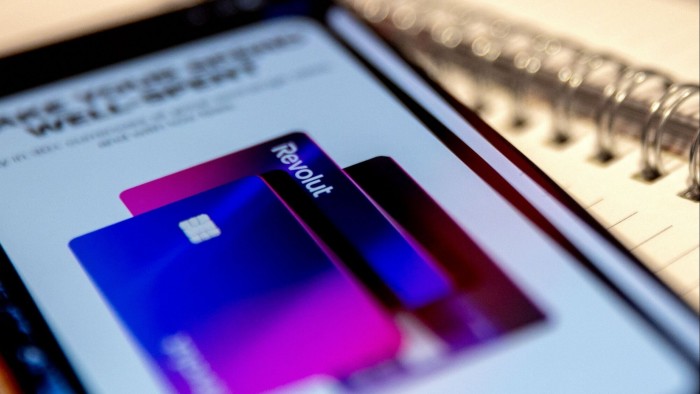 A smartphone screen displays the Revolut app with an image of two colourful credit cards, featuring the Revolut logo