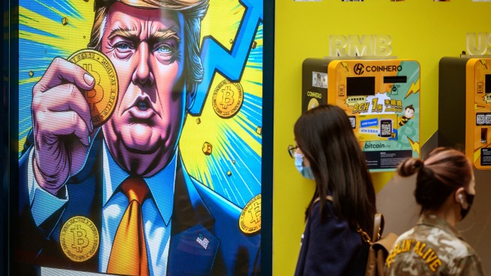 People walk past a cryptocurrency exchange office with a screen featuring US President Donald Trump holding cryptocurrency coins in Hong Kong