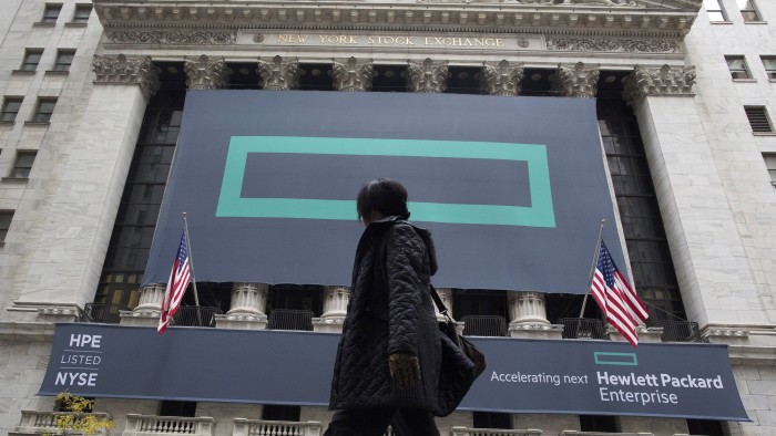 A person walks past the New York Stock Exchange, where large signs for Hewlett Packard Enterprise cover the facade