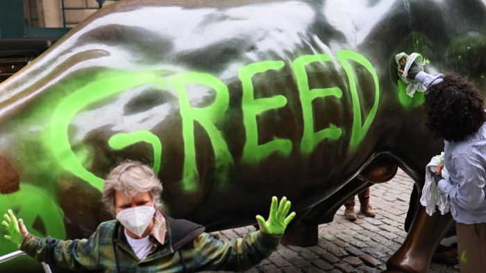 Climate activists next to a statue of a bull marked with the word ‘GREED’ in green paint