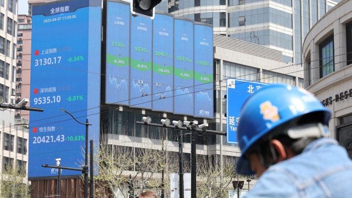 An electronic board in Shanghai displays stock indices. A person wearing a blue helmet is visible in the foreground.