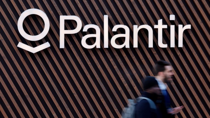 A man walks underneath a Palantir logo