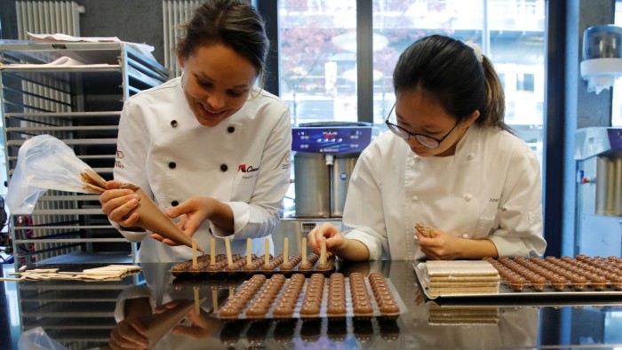Two employees of Barry Callebaut, dressed in white chef coats, prepare chocolates at a workstation