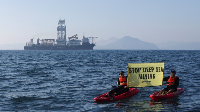 Greenpeace activists hold a yellow banner reading "STOP DEEP SEA MINING" while sitting in kayaks on the ocean