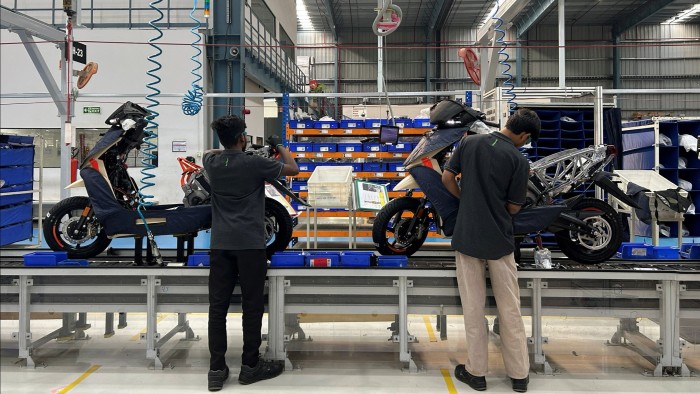 Two workers with their backs to the camera assembling two scooters on a production line