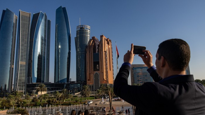 A visitor uses a smartphone to take a photograph of Etihad Towers in Abu Dhabi, United Arab Emirates