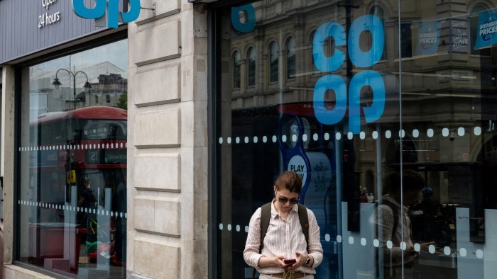 A pedestrian looks at a phone while outside a Co-op store in London, England