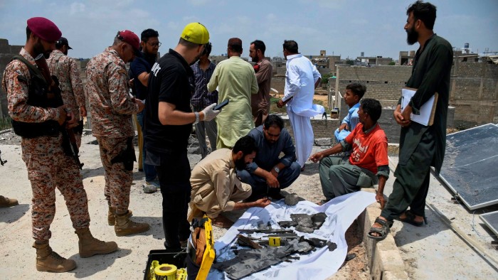 Pakistani paramilitary soldiers stand guard as investigators collect pieces of a suspected Indian drone in Karachi