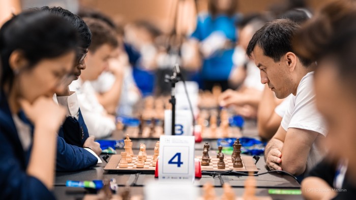 A view down a long row of chess players gazing over boards in a large hall