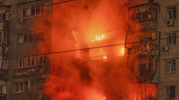 Flames and thick smoke engulf several floors of a damaged apartment building at night after a missile strike.