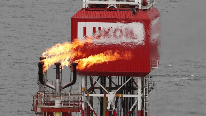 A Lukoil sign on an oil platform with gas flaring at sea.