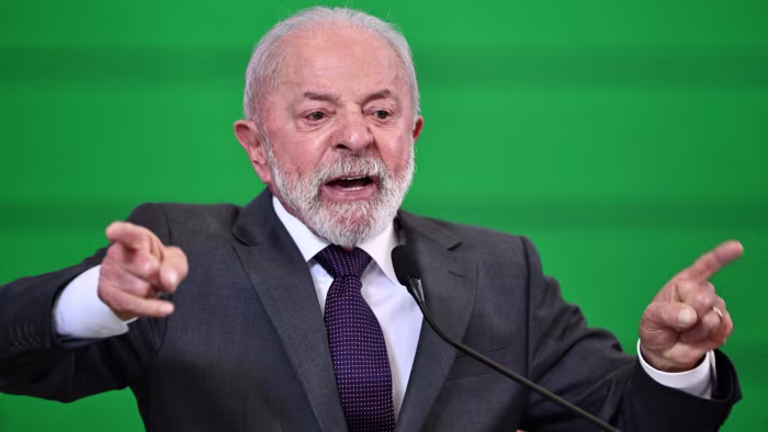 Luiz Inacio Lula da Silva gestures emphatically while speaking at a podium against a green background.
