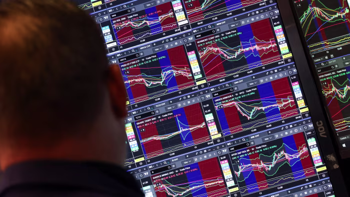A trader looks at multiple monitors displaying stock charts and market data at the New York Stock Exchange.