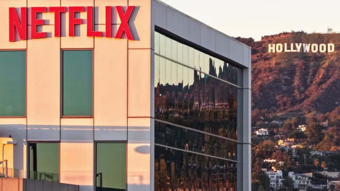 The Netflix logo on a studio building with the Hollywood sign visible in the distance on a hillside.