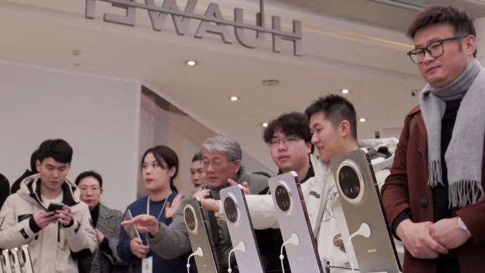 People examine Huawei Mate 70 smartphones. Several of them are observing or interacting with the devices.