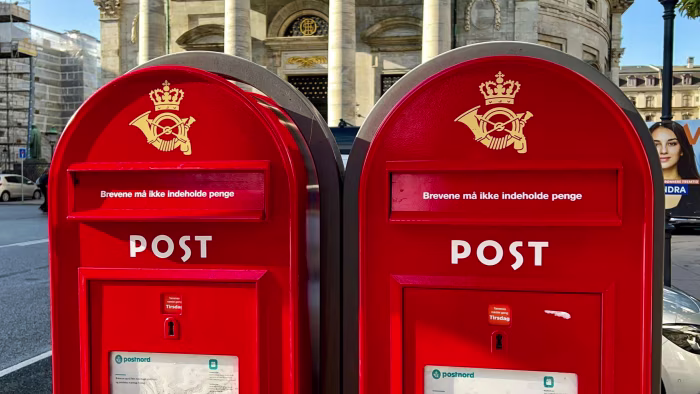 Two red Danish mailboxes with a gold crown and posthorn stand in front of a historic building in Copenhagen.
